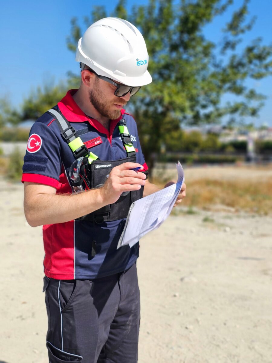 Construction worker in safety gear reviewing documents at a work site on a sunny day.