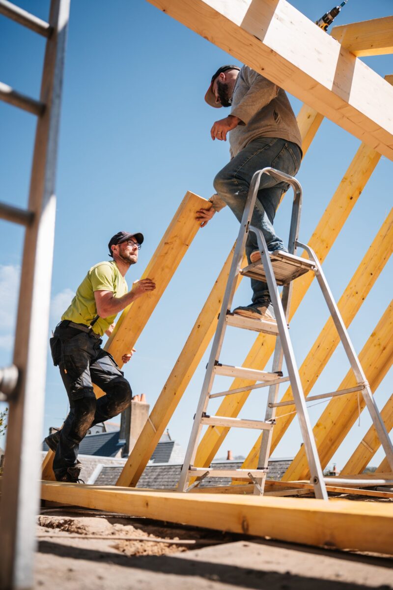 A dedicated carpenter using a tape measure on a house framework outdoors.