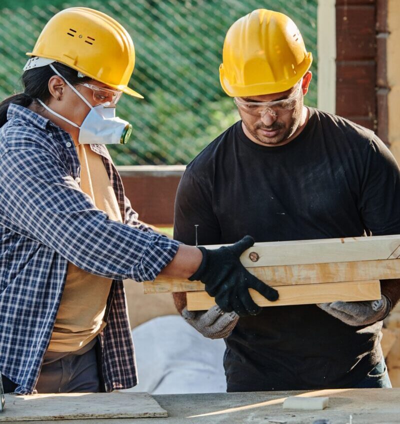 Two construction workers in hard hats collaborating at an outdoor site.