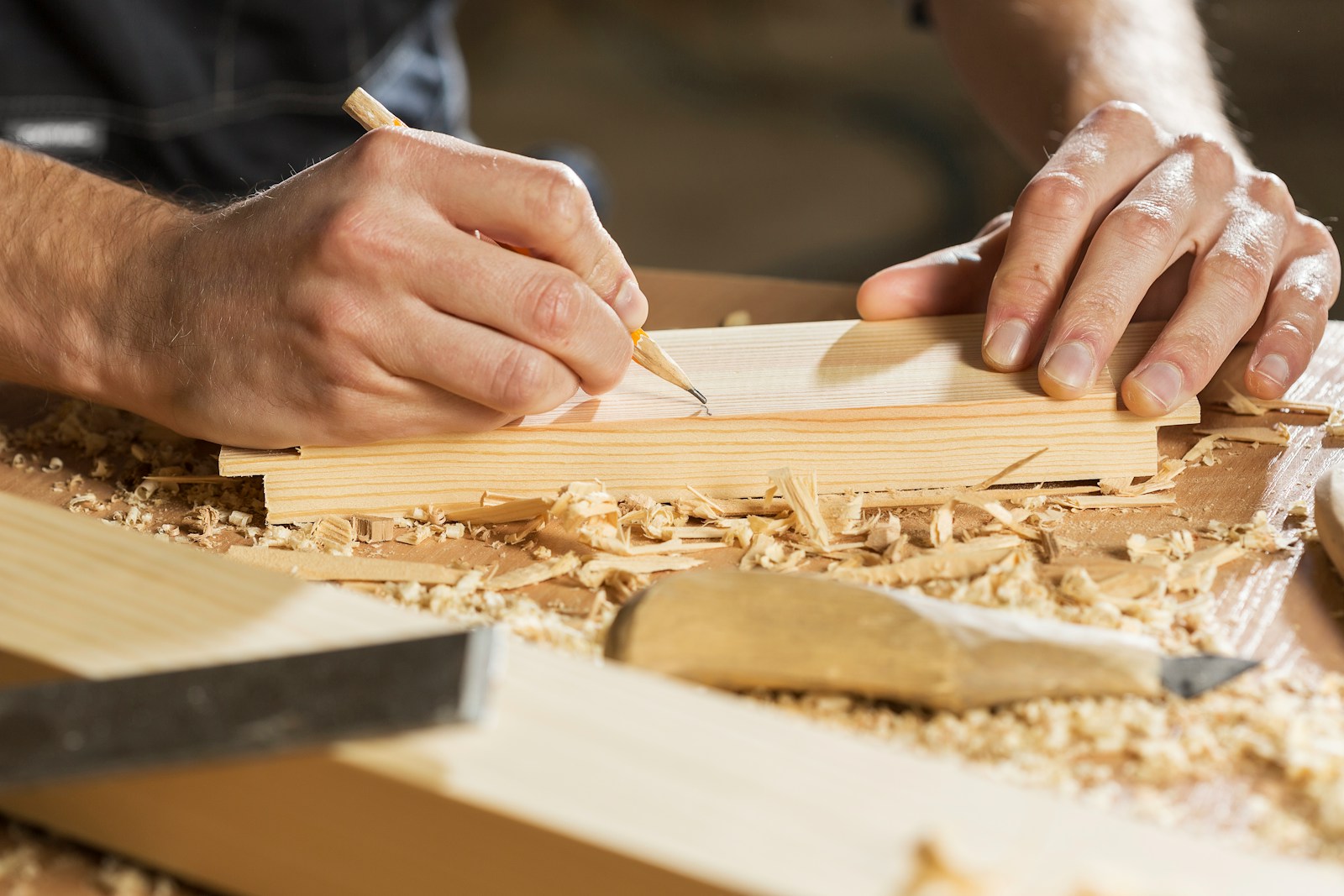 A person marking a line on a wooden board with a pencil